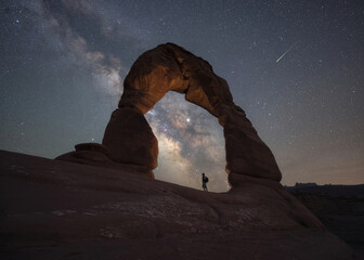 Hiker standing under Delicate Arch and the Night Sky