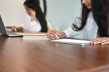 Cropped shot woman working on mockup digital tablet with stylus pen and colleague on background.