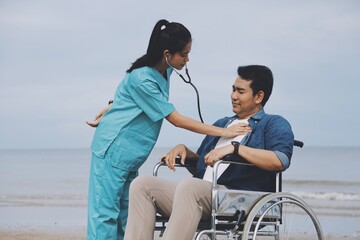 Young Asian man sitting in wheelchair ,Nurse and young man on the beach