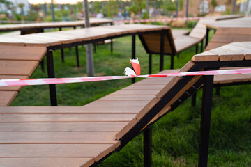 closed sports playground with wooden benches in a residential area, in a park, near the shopping center and deserted streets are sealed off with a barrier tape that prohibits passage during quarantine