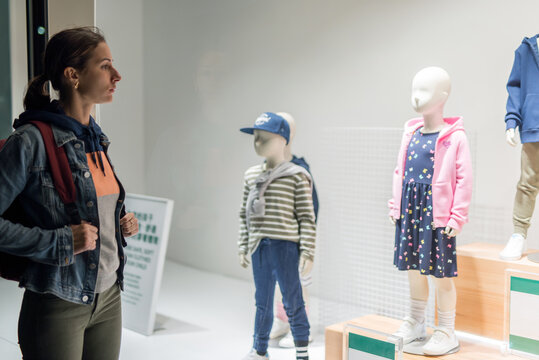 Young woman stands near kid's wear store window.