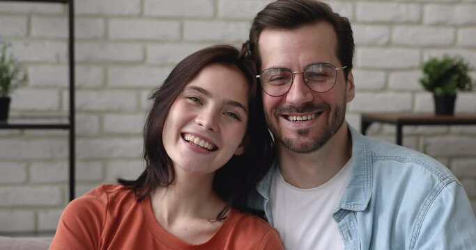 Pretty couple in love sit together indoor smile looking at camera enjoy distant videocall event communication with friends, happy homeowners young family portrait, rented flat and independence concept