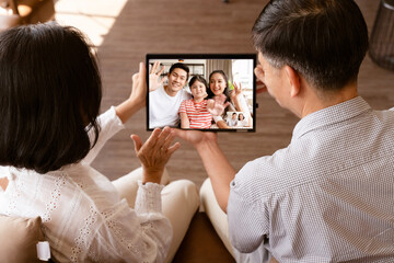 Scene of Asian family make a video conference call by tablet during self isolation at home while covid 19 epidemic. Holiday blues pandemic for many family changed lifestyle meet up with online.