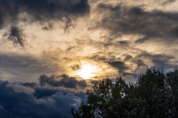 Dramatic sunset with bright yellow sun breaking through the clouds behind a tree in a stormy rainy day
