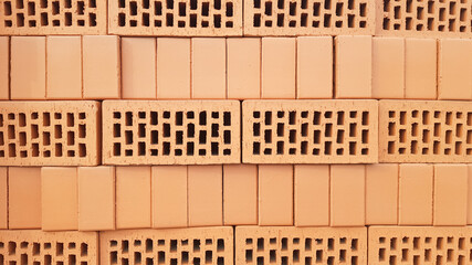 Red brick background with holes. Red perforated brick with rectangular holes. Rough texture of rows of red light bricks. View of the corrugated side and perforated upper surfaces of the clay brick.