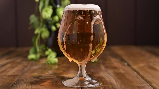 Beer. Cold Craft light Beer in a glass with water drops. Pint of Beer close up on a wooden background. Beer is pouring from the bottle. Border design. High quality 4k footage