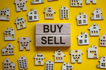 Wooden blocks form the words 'buy, sell', miniature wooden houses. Beautiful yellow background, copy space. Business concept.