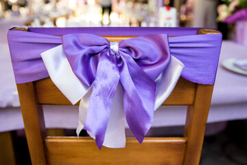 In the photo we see chairs decorated with lavender lilac ribbons. Indoor wedding ceremony. Lavender-style location prepared.