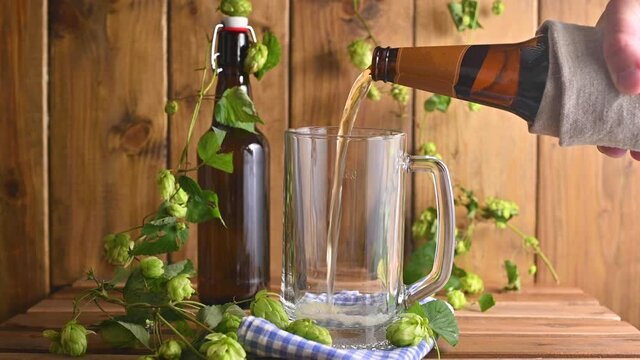 Beer. Cold Craft light Beer in a glass with water drops. Pint of Beer close up on a wooden background. Beer is pouring from the bottle. Border design. High quality 4k footage