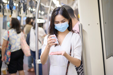 A young woman wearing protective mask in subway is using alcohol to wash hands, travel under Covid-19 pandemic, safety travels, social distancing protocol, New normal travel concept