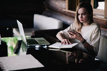 Young slender girl at the restaurant table works behind a laptop