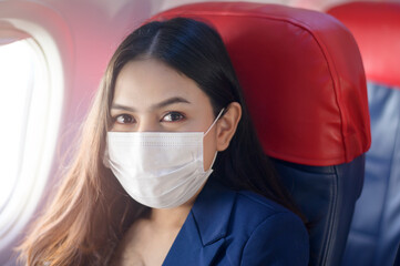 A young businesswoman is wearing protective mask onboard in the aircraft, travel under Covid-19 pandemic, safety travels, social distancing protocol, New normal travel concept