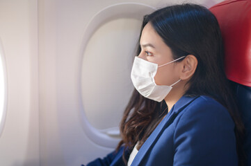 Fototapeta na wymiar A young businesswoman is wearing protective mask onboard in the aircraft, travel under Covid-19 pandemic, safety travels, social distancing protocol, New normal travel concept