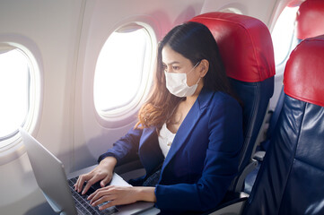 A young businesswoman wearing face mask is using laptop onboard, New normal travel after covid-19 pandemic concept
