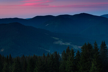 Amazing landscape in the layers of mountains at the dusk. View of colorful sky and hills covered by forest. 
