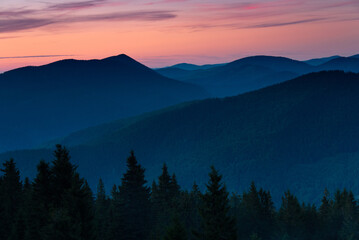 Amazing landscape in the layers of mountains at the dusk. View of colorful sky and hills covered by forest.