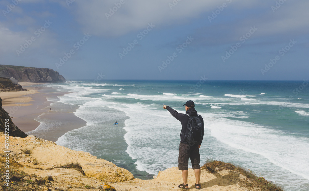 Wall mural a tourist on a rocky shore looks in the distance at the raging ocean and surfers. atlantic ocean. po