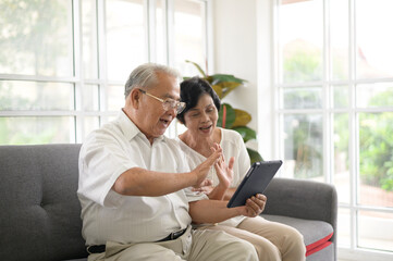 An Asian happy seniors elderly are video calling , relax at home, smiling healthy senior retired grandparents, older grandparent technology concept