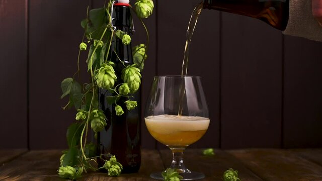 Beer. Cold Craft light Beer in a glass with water drops. Pint of Beer close up on a wooden background. Beer is pouring from the bottle. Border design. High quality 4k footage