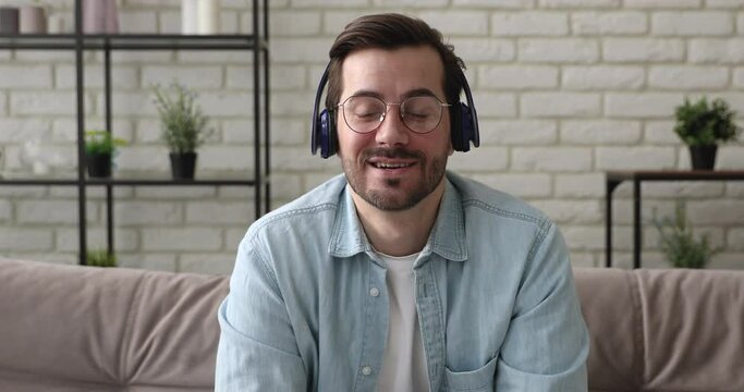 Head shot of 35s male applicant pass job interview answer question distantly wear headphones use internet connection computer feels confident. Video call activity, freelance telework from home concept