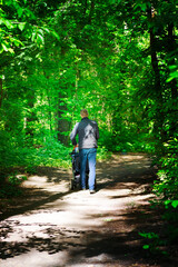 Obraz premium Forest dirty road and walking man with baby carriage in a sunny summer day.