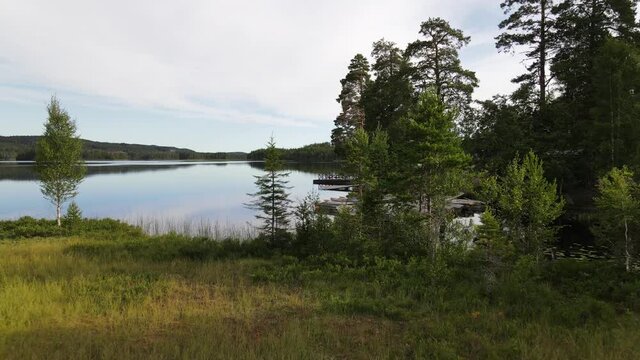 Drone flying low and close to trees and on over a calm, mirrorlike lake one sunny summer morning in Säfsen, Sweden. Small rowing boats in background. Aerial 4K footage.