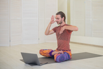 A young male yogi practices and teaches yoga online on a laptop in the Studio, performing and...