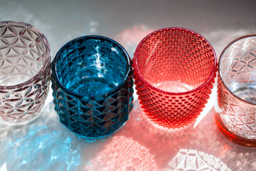 Four glass candlesticks with sun glow and patterned shadows. Colored glass products of various shapes and colors close up
