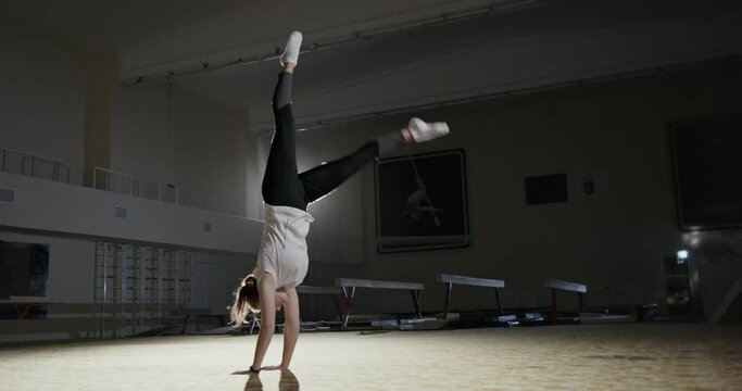 Full body slim sportswoman practicing handstand exercise during gymnastic workout in illuminated gym