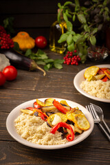 Porridge couscous with baked vegetables, zucchini and onions, bell peppers and eggplants with spices, plate with food on a dark wooden background