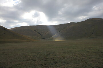 Portentous ray of sunshine that pierces the cloudy sky and illuminates a small part of the plain in the shade