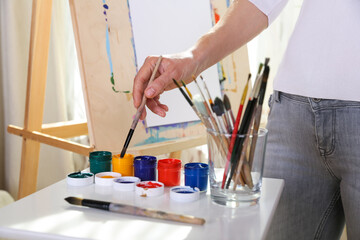 painter's hand holds brush on the background of the easel