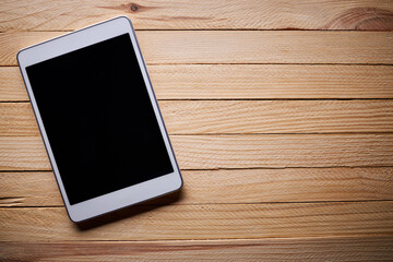 white digital tablet over wooden desk workplace. above view. mobile service concept. dark mood