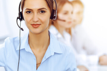Call center operators. Focus on beautiful business woman using headset in sunny office - obrazy, fototapety, plakaty