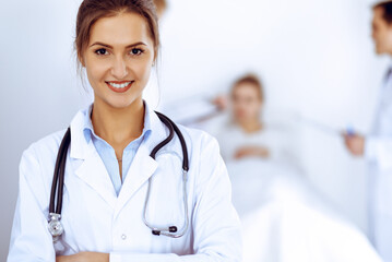 Fototapeta premium Female doctor smiling on the background with patient in the bed and two doctors