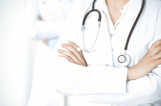 Unknown woman-doctor standing straight with arms crossed in clinic, close-up. Medical team ready to stop coronavirus pandemic. Medicine concept