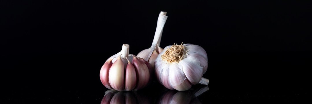 Tr&ecirc;s bulbos de Alho com pil&atilde;o ao fundo sobre a mesa espelhada de fundo negro.