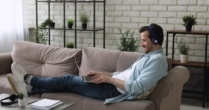 Man sit leaned on couch wear headphones put laptop on laps start video call talk greeting business partner, due corona virus business people lead negotiations use modern tech videocall, event concept