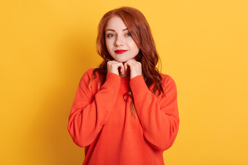 Charming attractive red-haired young female with cute expression, looking at camera, smiling cheerfully, feeling relaxed and happy, wearing casual orange sweater.