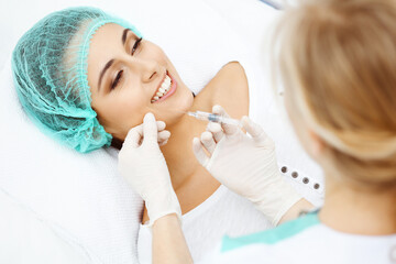 Professional cosmetologist making injection in face, lips. Young woman gets syringe with filler for...
