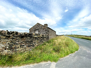 Fototapeta na wymiar An old stone barn, with grass verges, by the side of the Skipton to Clitheroe road near, Lothersdale, Keighley, UK