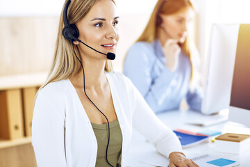 Portrait of call center operator at work in sunny office. Group of people in a headset ready to help customers. Business concept