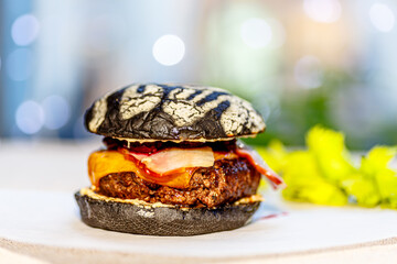 A black Burger with bacon and berry sauce is on the table.
