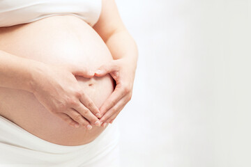 Pregnant woman hold heart-shaped hands on her baby bumps skin. Copyspace for your text.