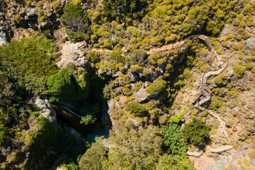 Aerial view of a waterfall in a narrow gorge next to winding wooden steps (Richtis Gorge, Crete, Greece)