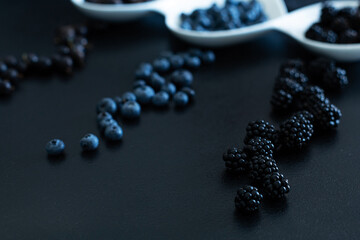 Set of different types of black berries in a white plate on a black table. Stylish seasonal vitamins