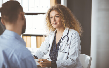 Female doctor and male patient discussing current health examination while sitting in clinic....
