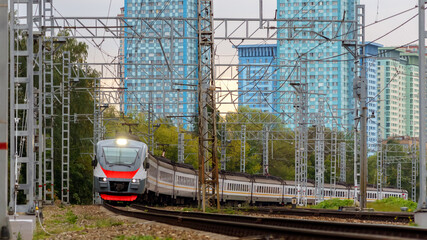 Naklejka premium Passenger train arriving at the railway station in the city. Urban landscape, skyscrapers in the background.