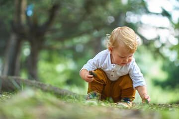 curious little child sitting in the forest studying and looking at different objects in the soil