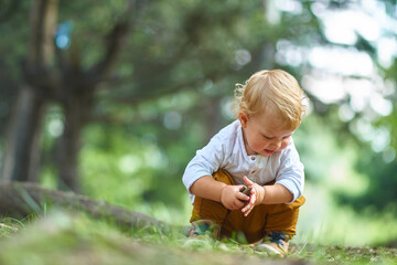 curious little child sitting in the forest studying and looking at different objects in the soil